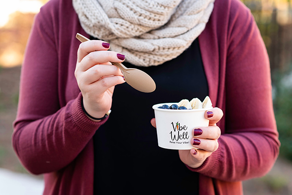 A hand begins to dip a spoon into a custom printed ice cream cup topped with fruit.